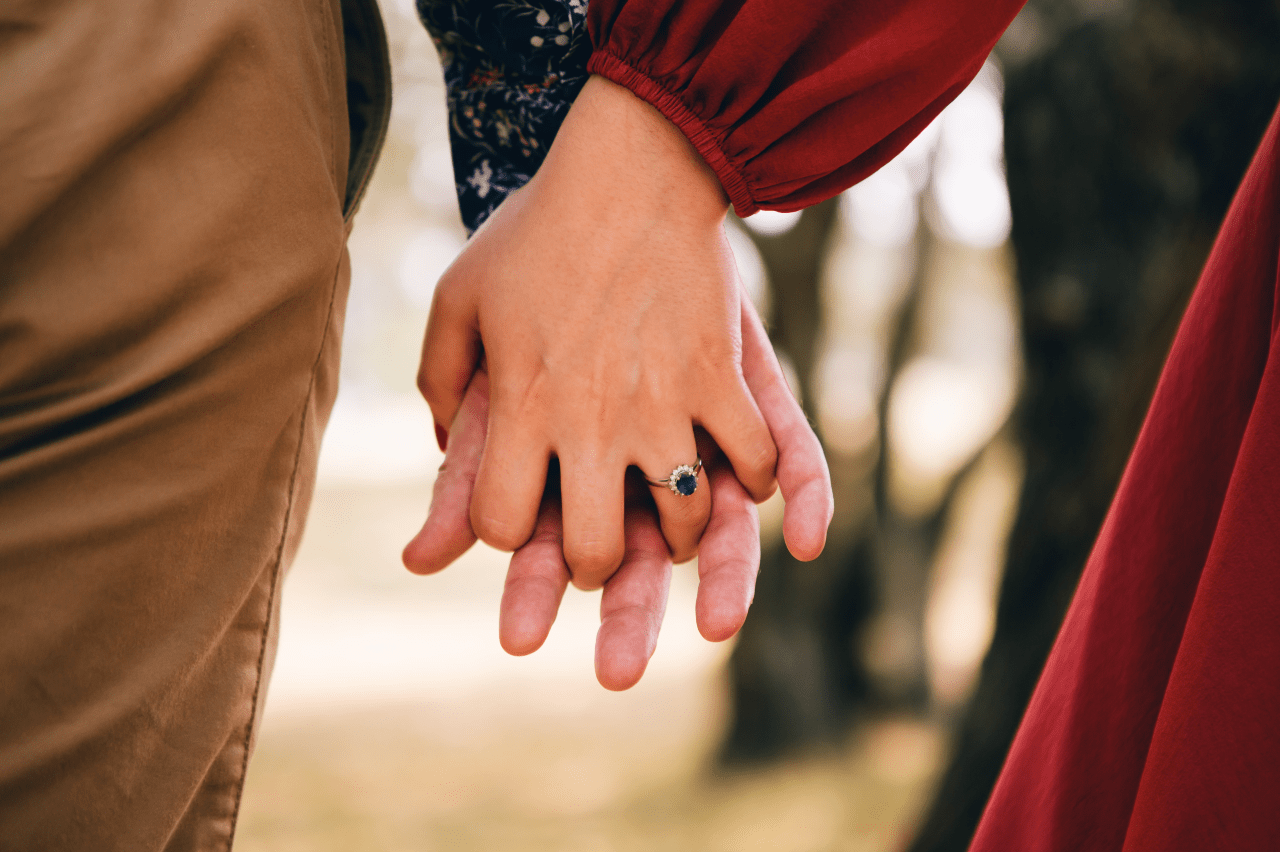 Two hands holding each other, the woman’s hand wearing a sapphire engagement ring