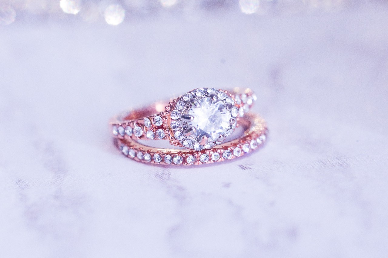 A rose gold wedding band and halo engagement ring on a white background