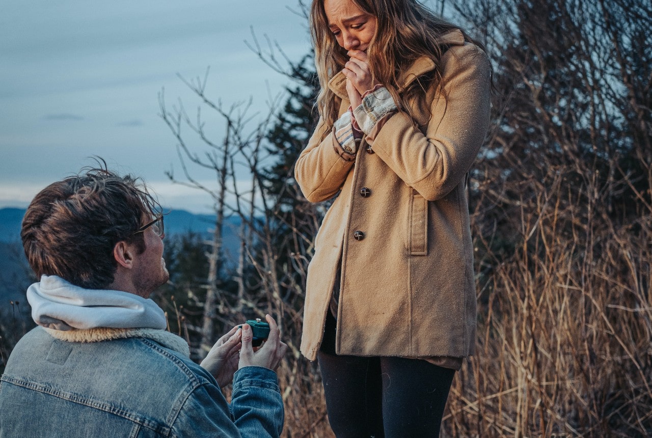 A man proposing to a woman on a hike. She is surprised and happy