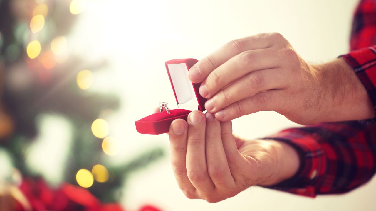 An open red ring box with an engagement ring presented to someone