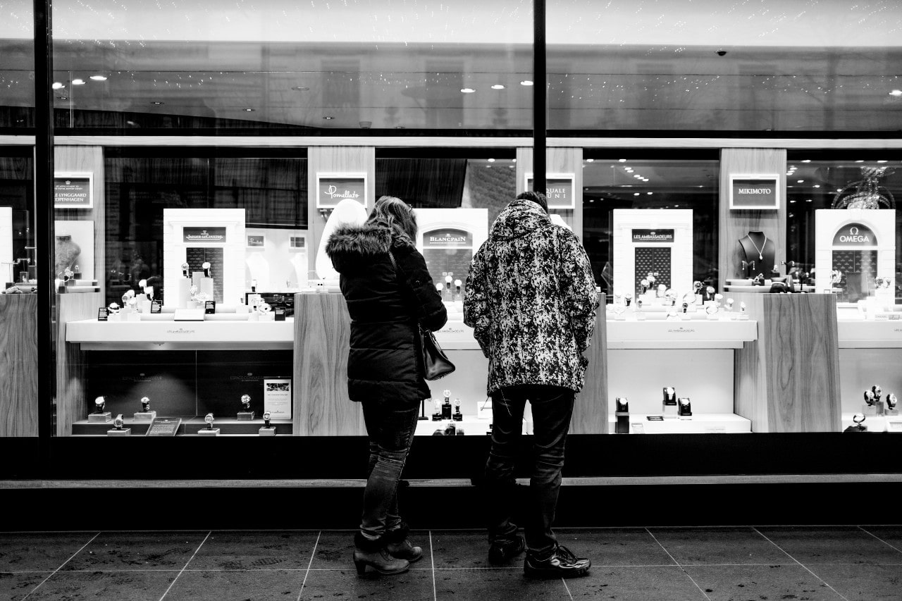 A couple peers into the window of a closed jewelry store while on an evening stroll