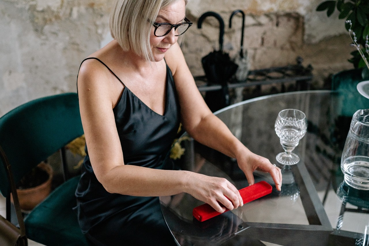 A woman sitting at a table opening a red necklace box