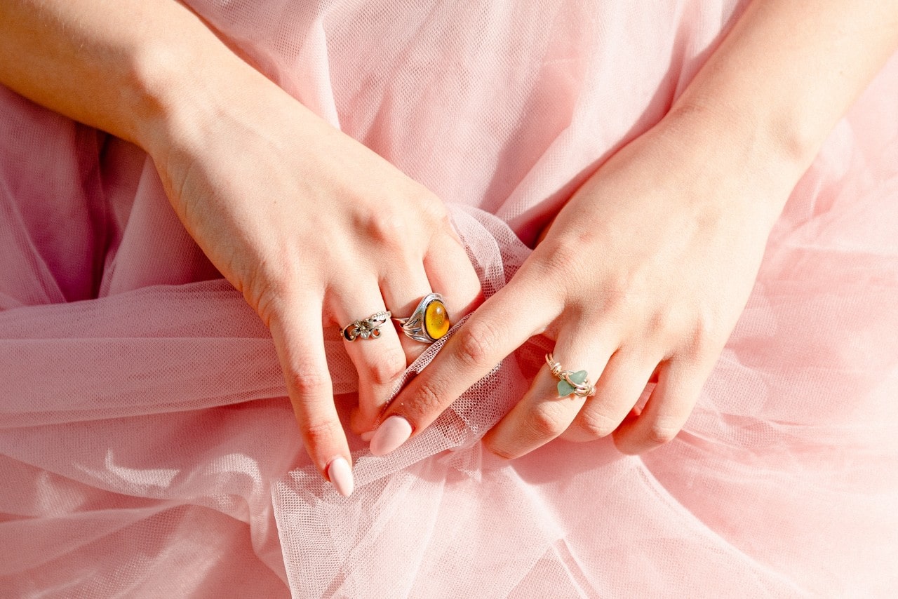A woman wearing pink and crossing her hands over her dress and wearing various gemstone rings