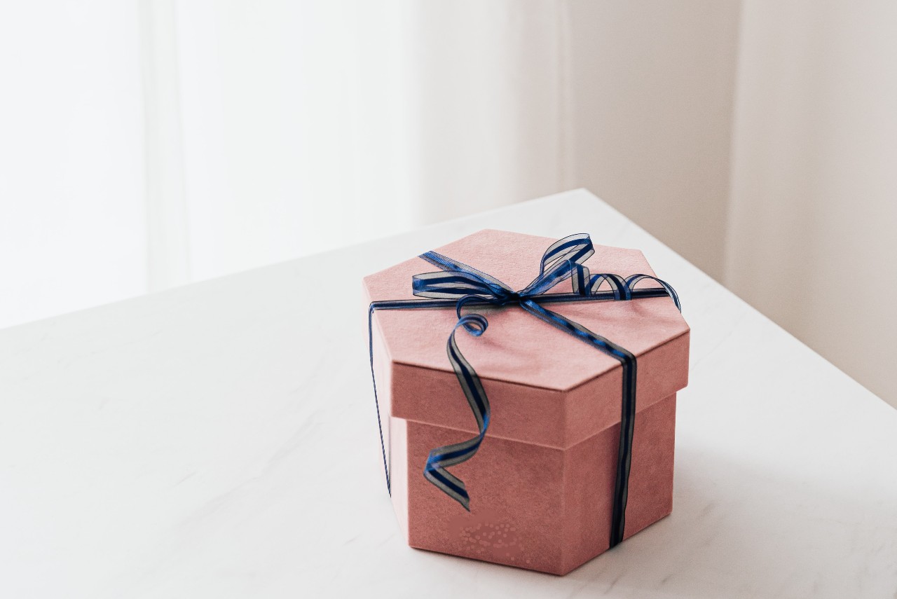 A pink gift box with a blue ribbon sitting on the corner of a white table