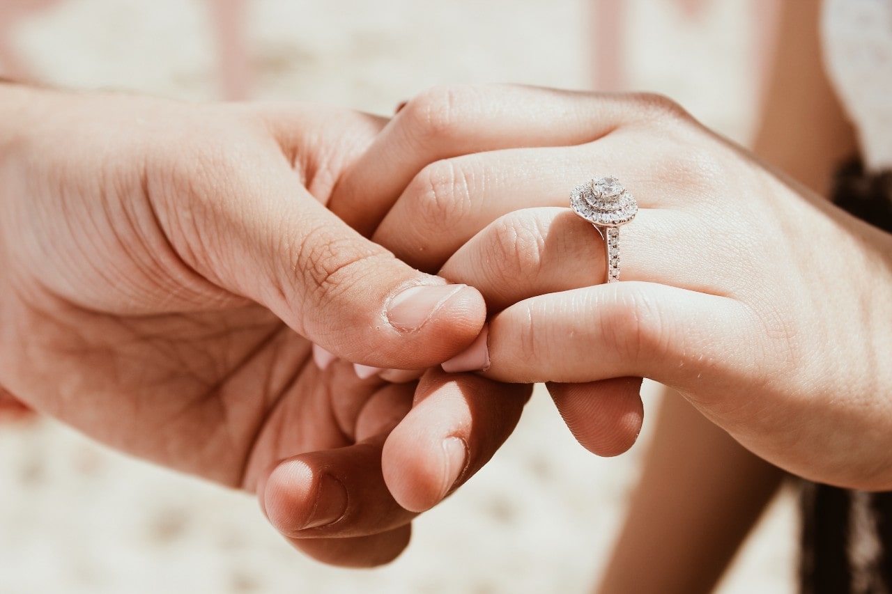 A man holds a woman’s hand, showing off her halo engagement ring