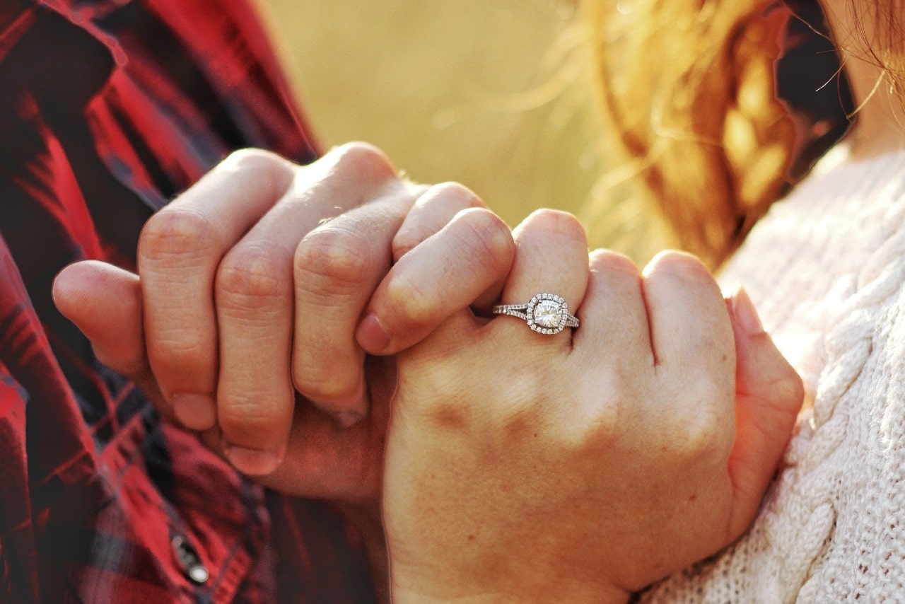 A man and woman link pinky fingers, showing off her engagement ring